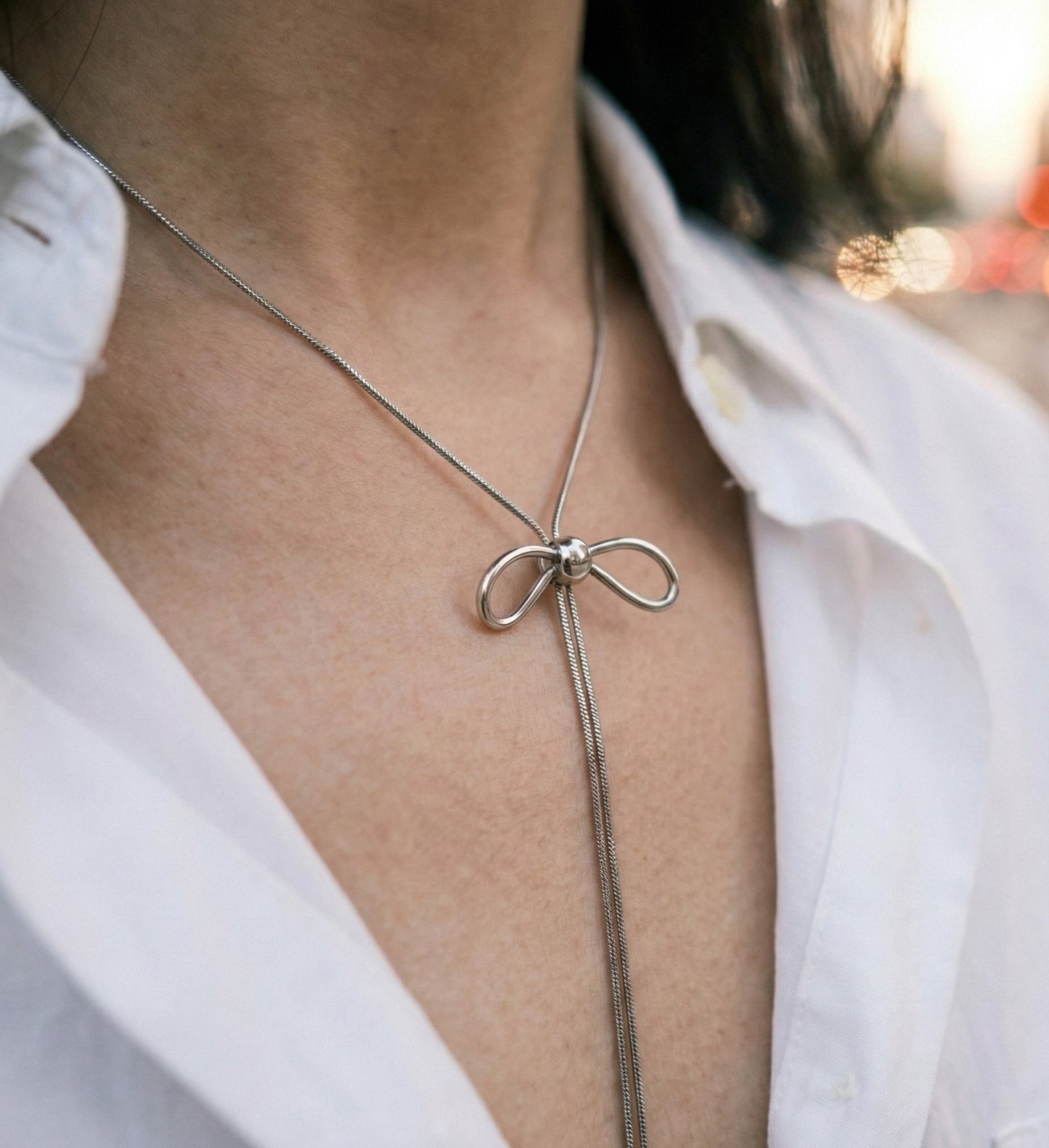 Woman wearing silver bow lariat necklace with white shirt - elegant office styling