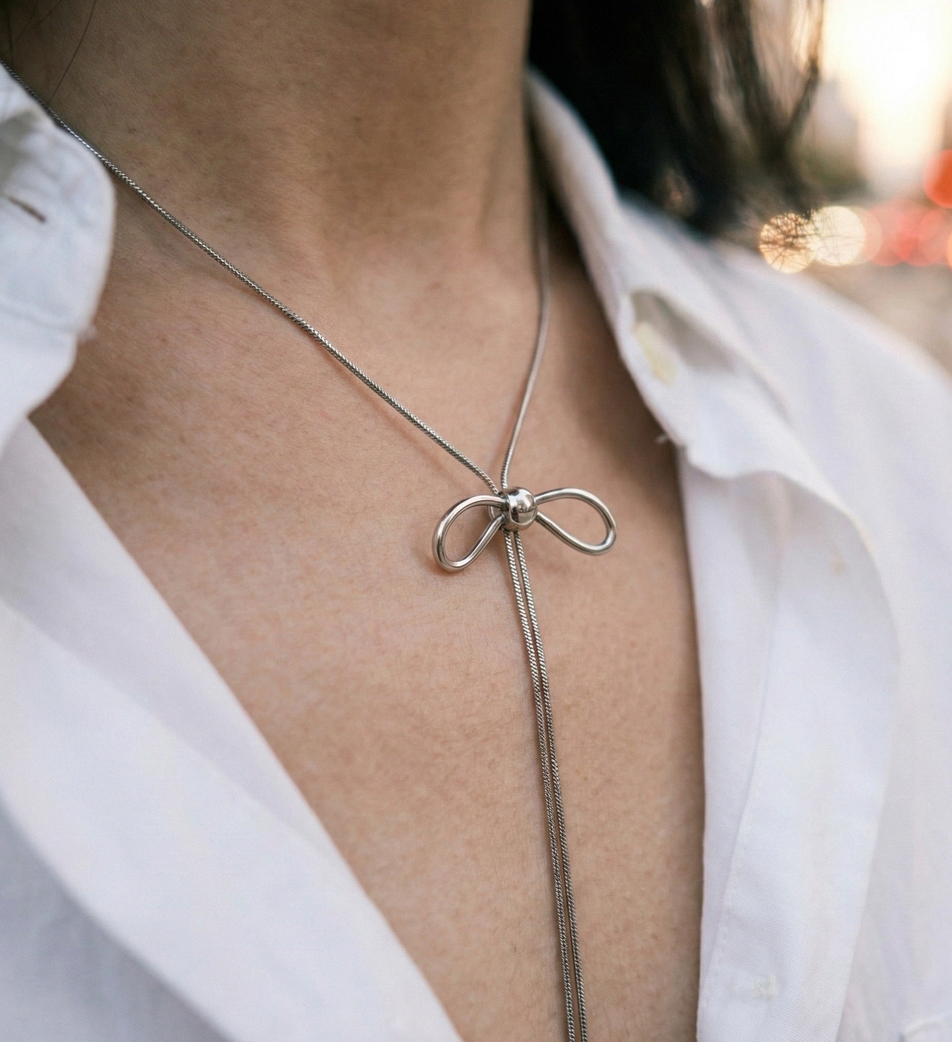 Woman wearing silver bow lariat necklace with white shirt - elegant office styling
