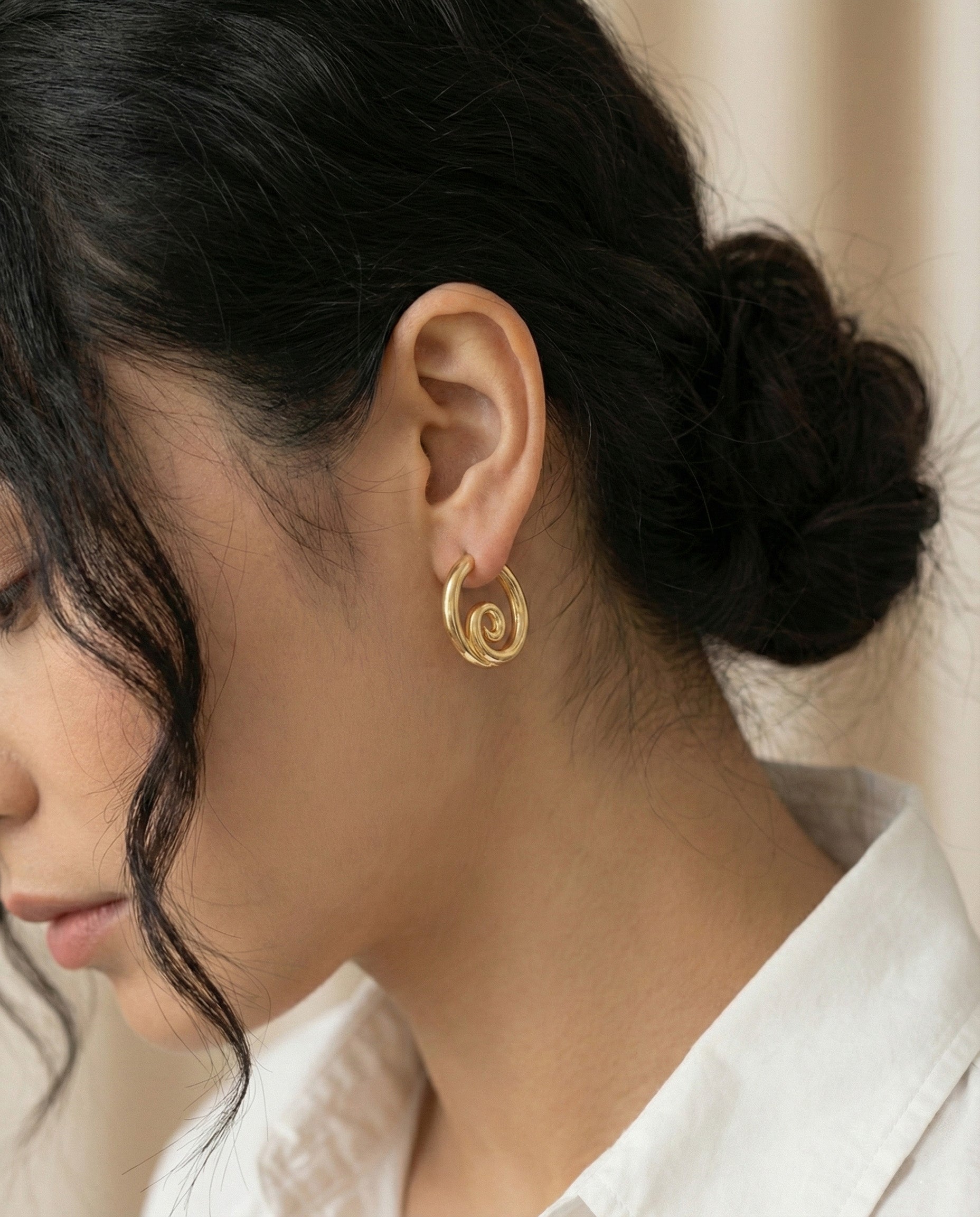 Model wearing gold spiral hoop earrings with white shirt - side profile view