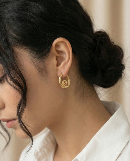 Model wearing gold spiral hoop earrings with white shirt - side profile view