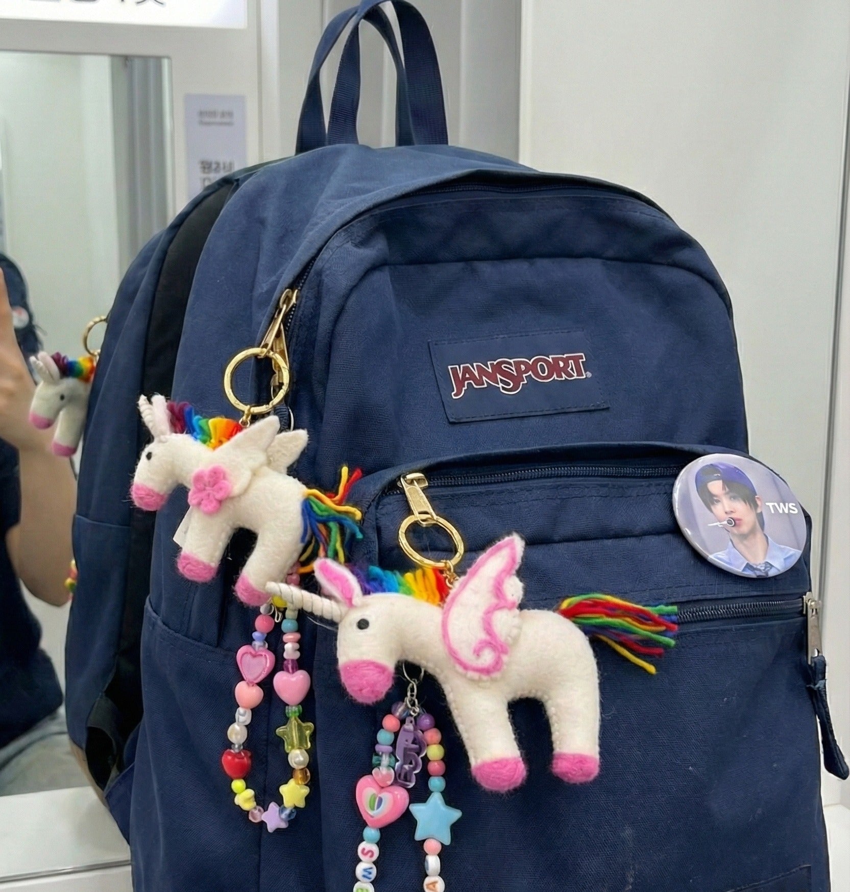 Navy JanSport backpack decorated with rainbow unicorn keychains and colorful beaded charms for bag decoration