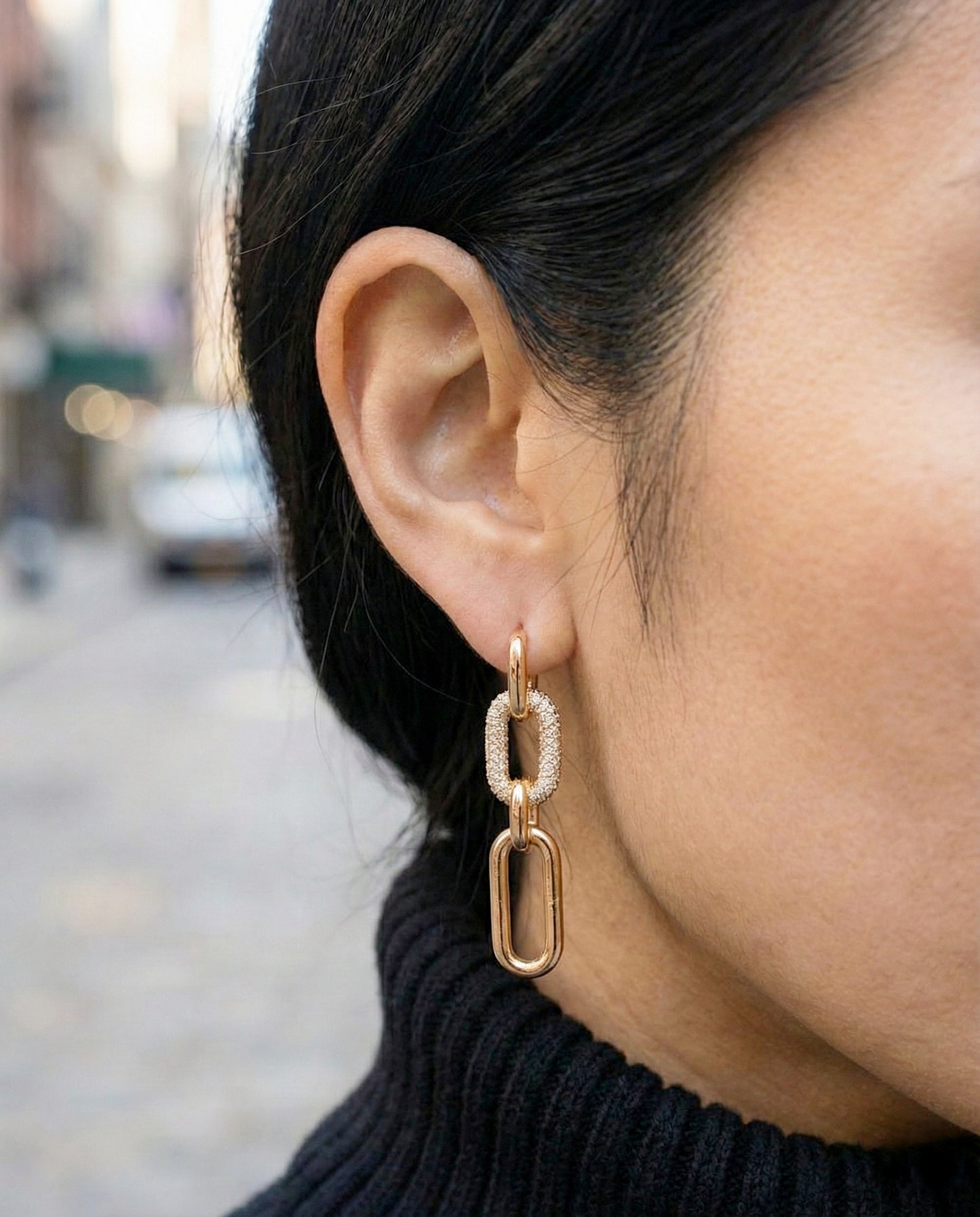 Woman wearing gold chain link drop earrings with black turtleneck sweater, showing face-framing effect