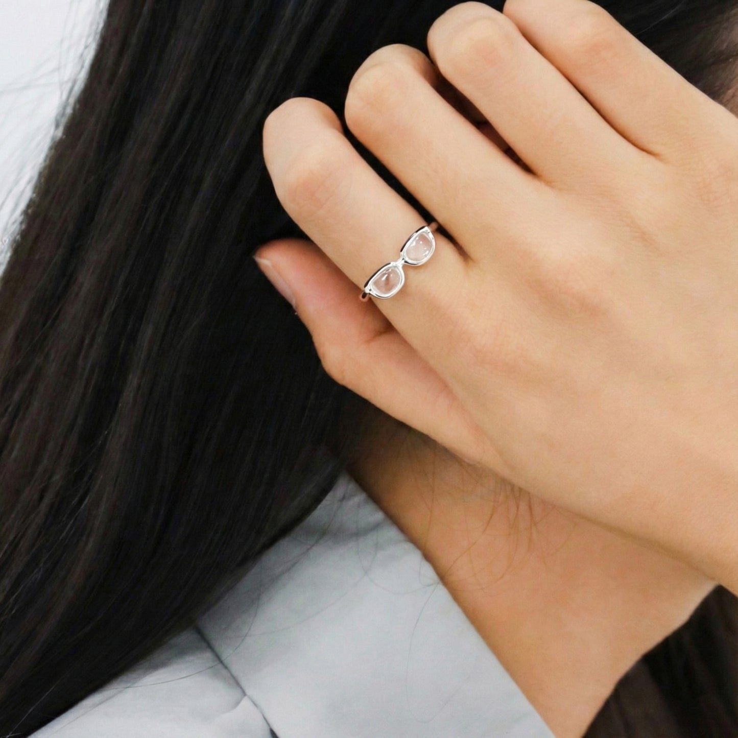 Side profile of woman wearing unique glasses-shaped silver ring on index finger against dark hair