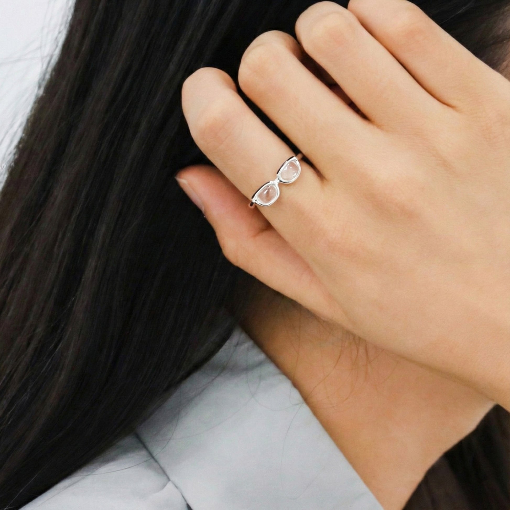 Side profile of woman wearing unique glasses-shaped silver ring on index finger against dark hair