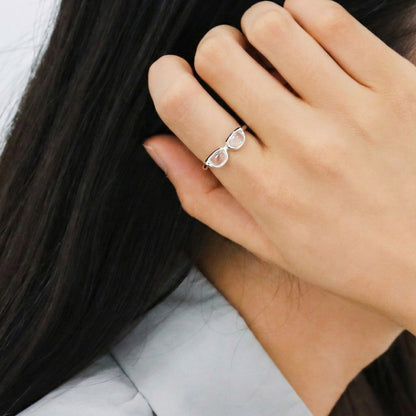 Side profile of woman wearing unique glasses-shaped silver ring on index finger against dark hair