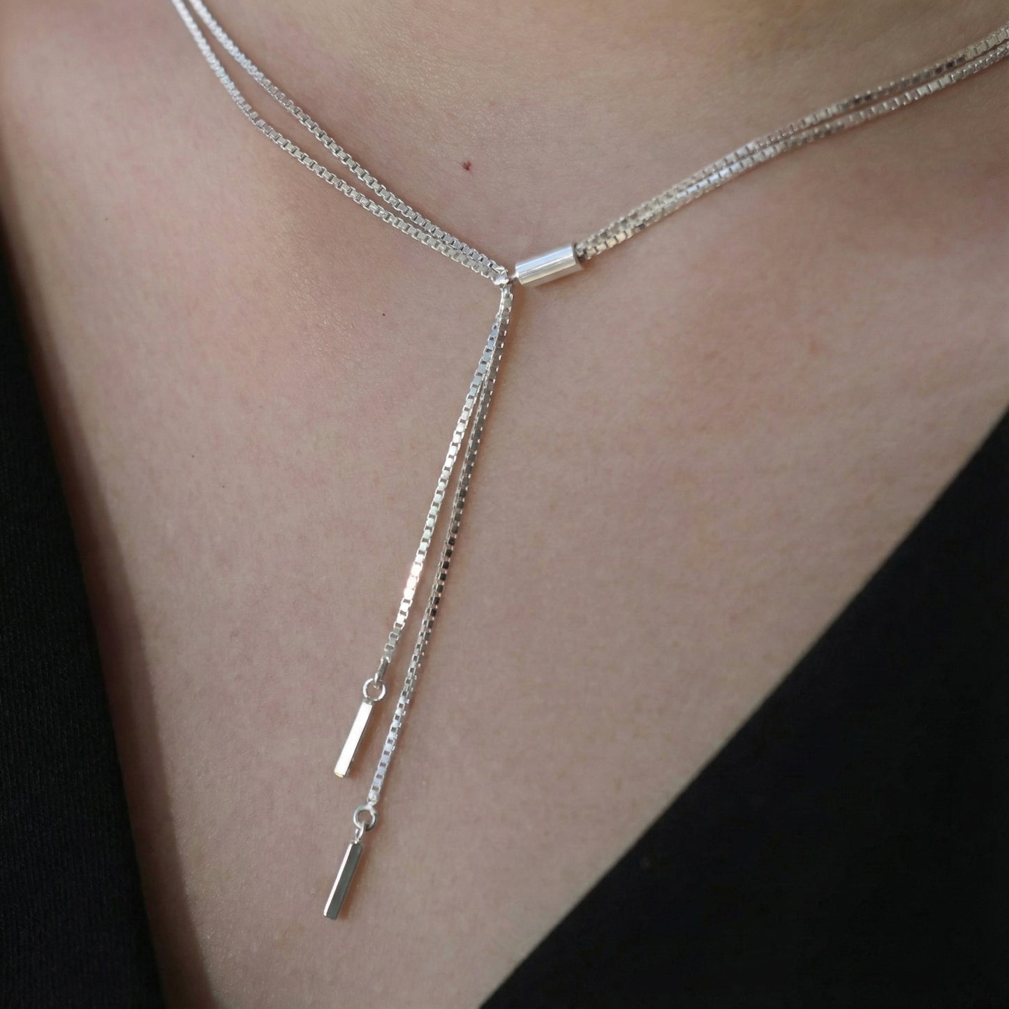 Close-up of silver Y-drop necklace with sleek stick pendants, layered around the neck