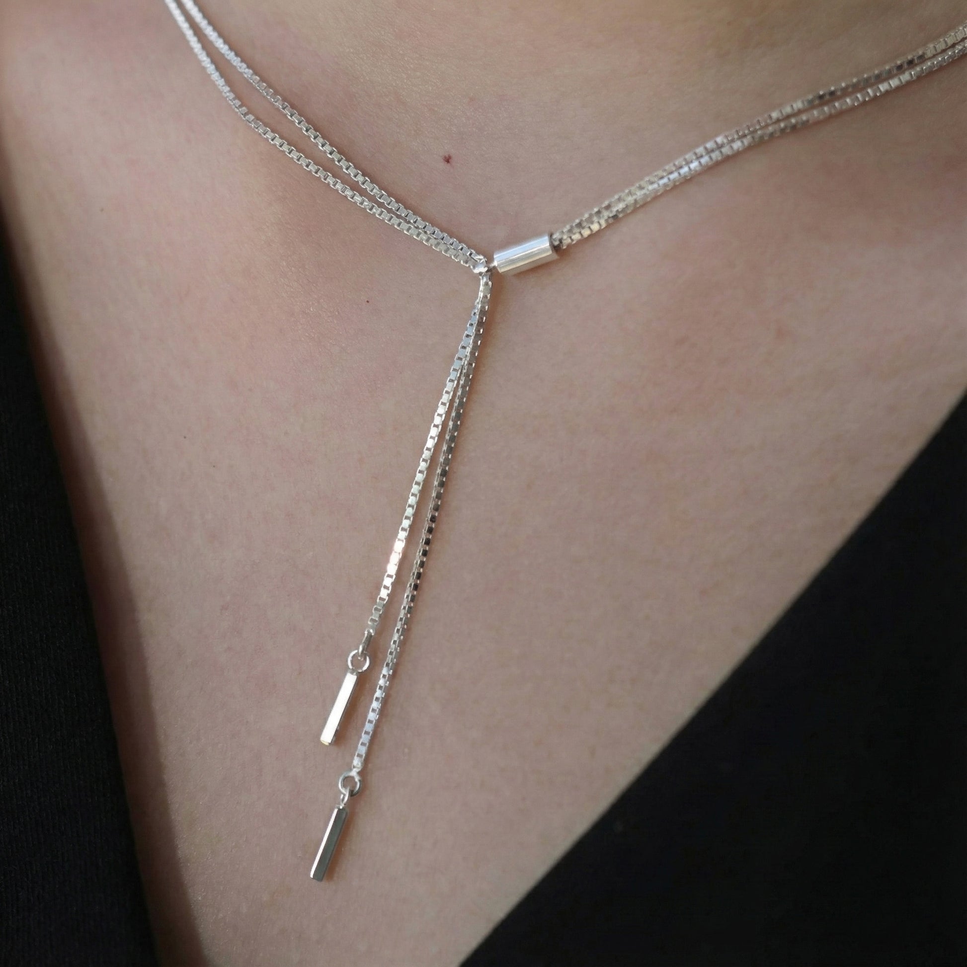 Close-up of silver Y-drop necklace with sleek stick pendants, layered around the neck