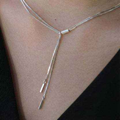 Close-up of silver Y-drop necklace with sleek stick pendants, layered around the neck