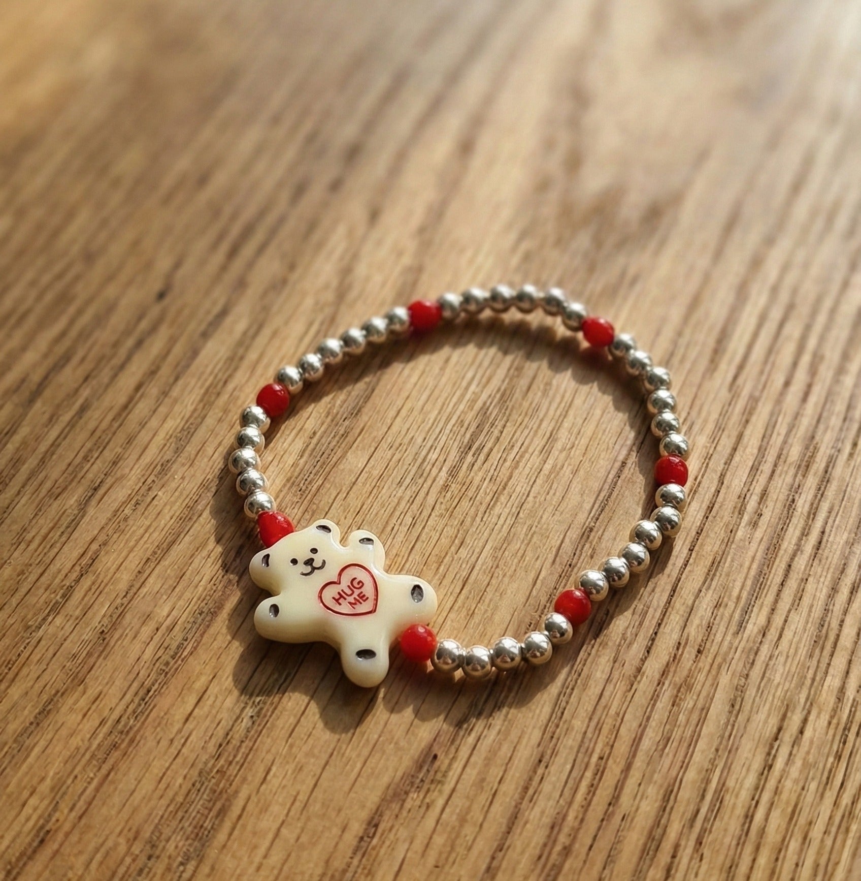 Milky white Hug Me bear silver ball bracelet with red seed bead accents on wooden background — Y2K kidcore aesthetic