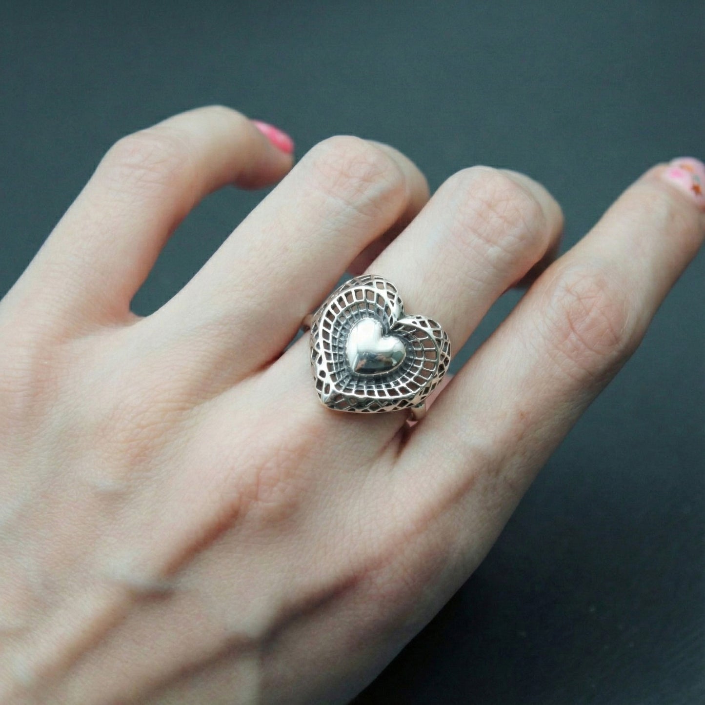  Front view of oxidized sterling silver heart ring on middle finger with pink nail polish