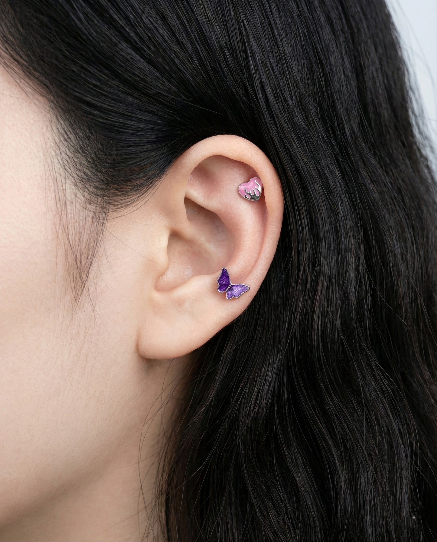 Purple melting heart piercing on helix with butterfly stud on lobe showcasing emo aesthetic ear styling