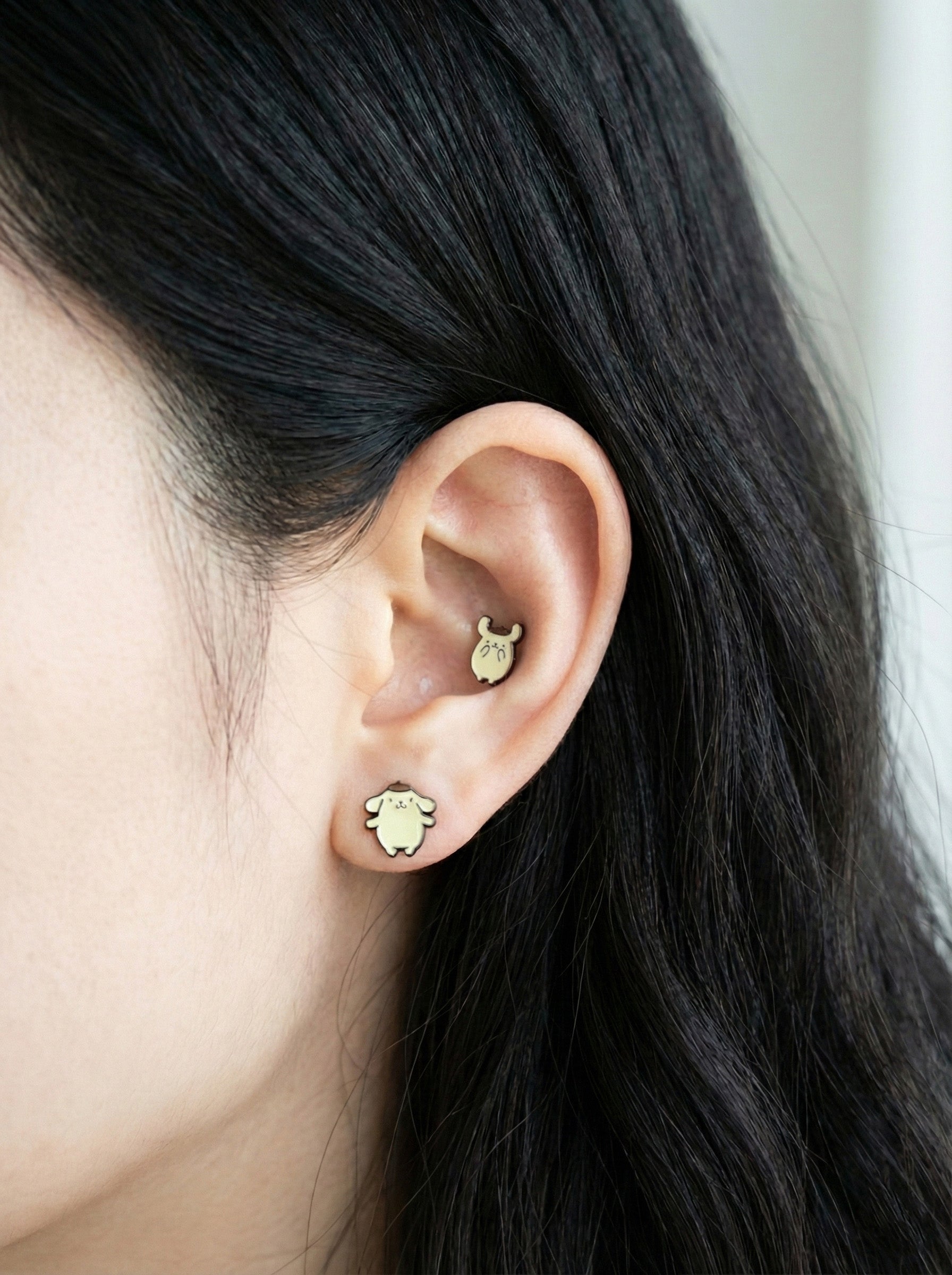 Side view of two Pompompurin piercings on ear lobe and conch showing dimensional brass setting