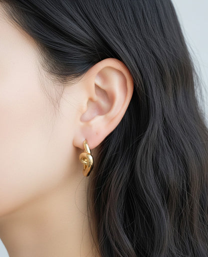 Side angle of gold love knot heart hoop earrings showing 3D twisted design, clicker closure