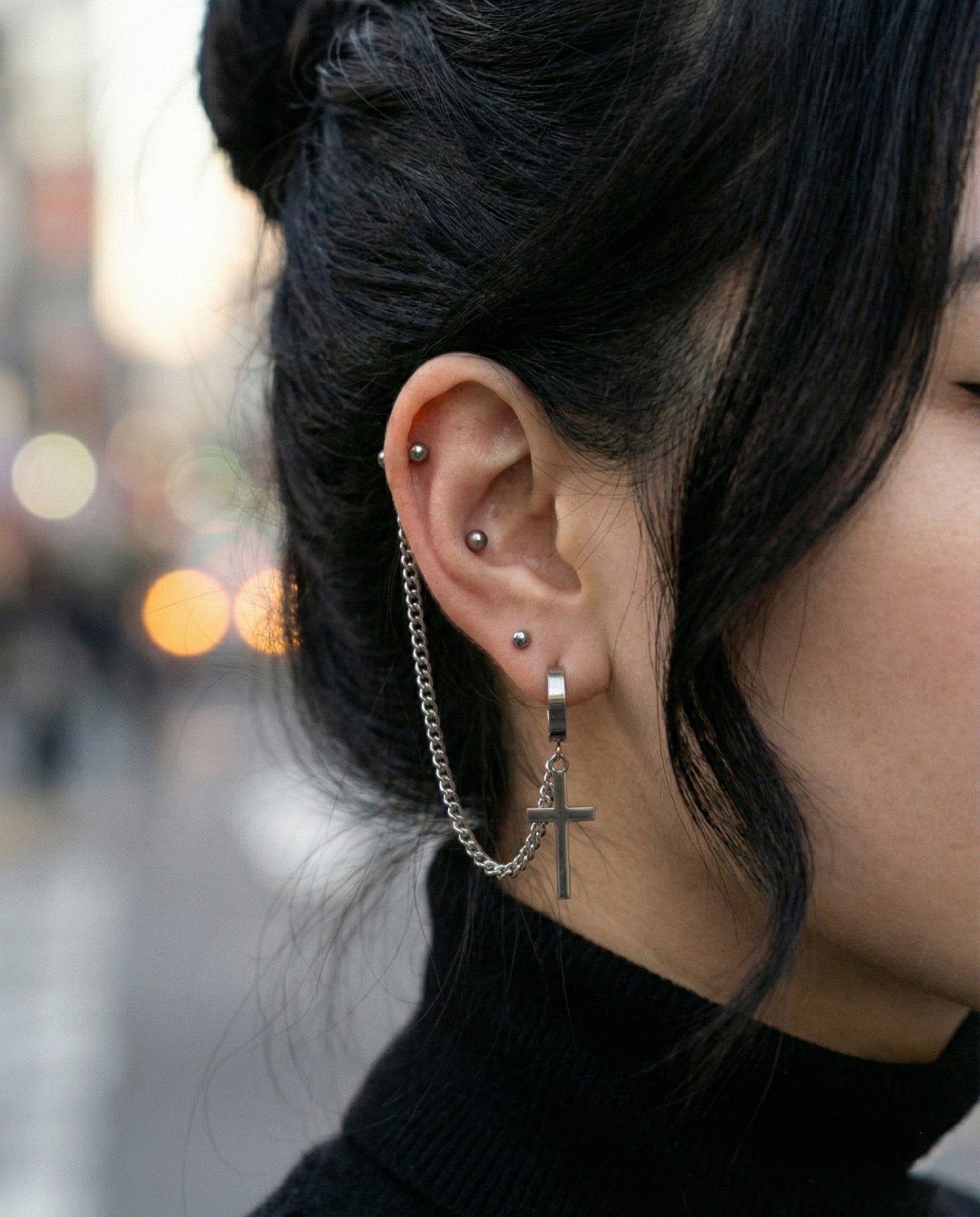 Close-up of diagonal chain piercing with cross charm on ear  