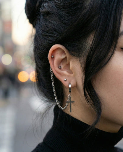 Close-up of diagonal chain piercing with cross charm on ear  