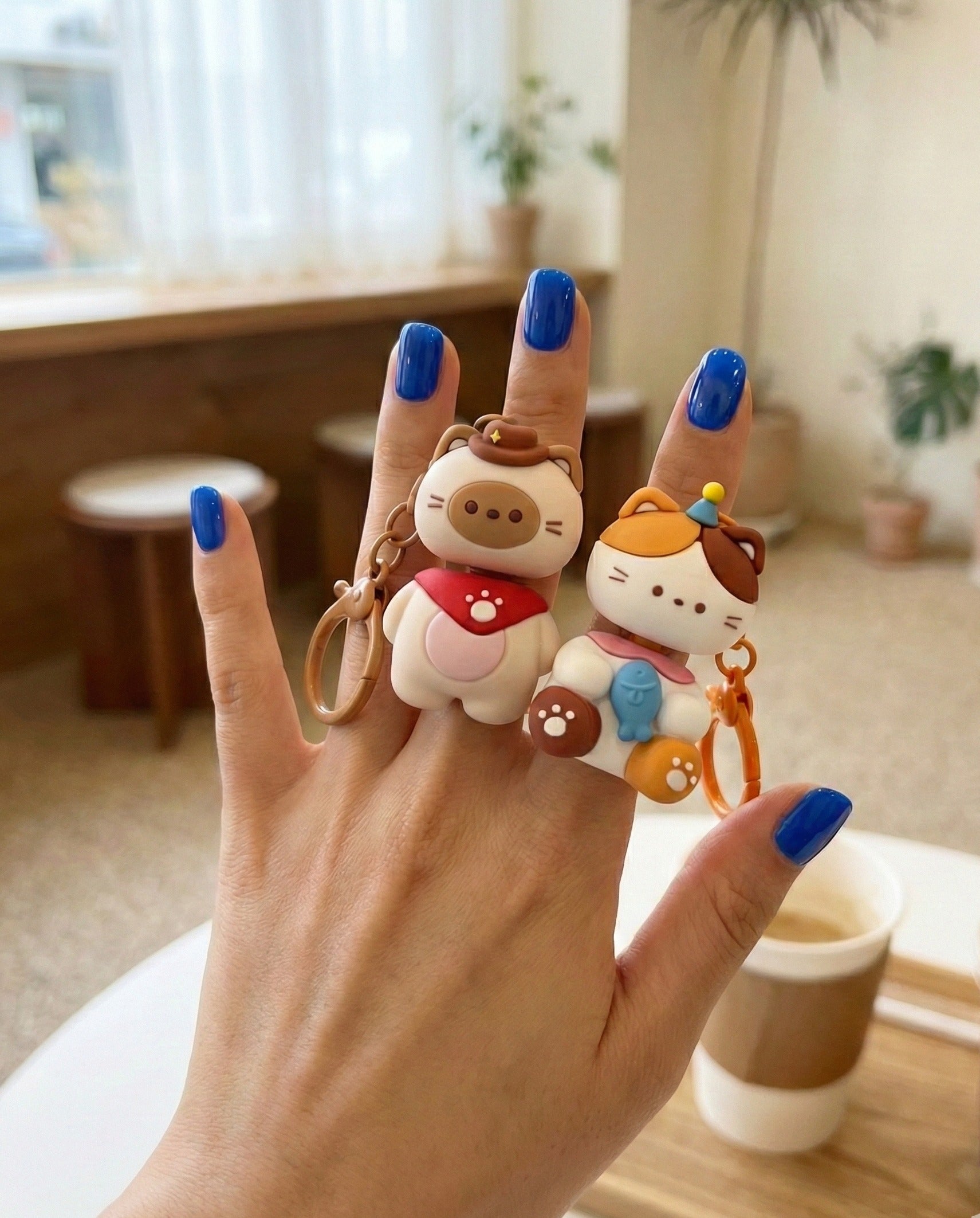 Hand holding two animal keycap keychains - cat and dog with glasses on finger rings