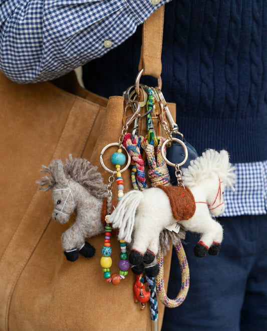 Two handmade horse keychains in grey and white hanging from beige canvas tote bag handles with colorful bead charms
