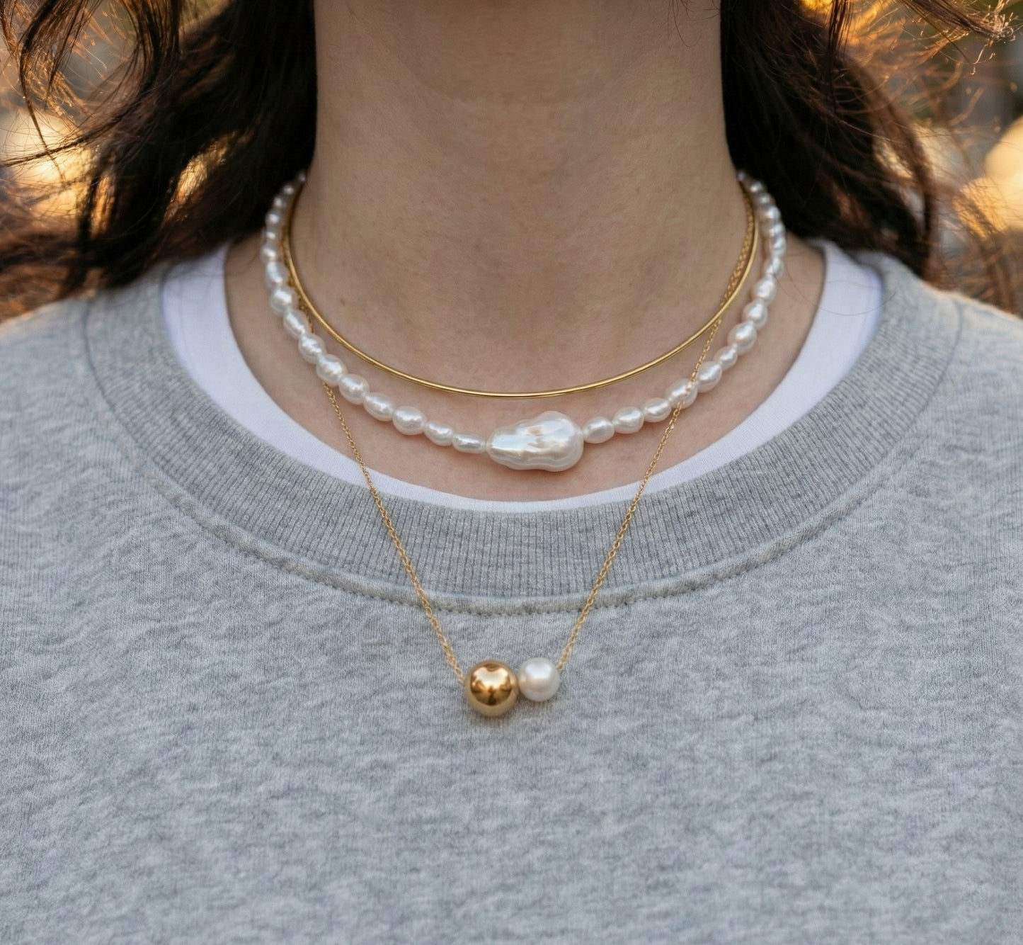 Woman wearing layered pearl and brass choker with gray knit sweater