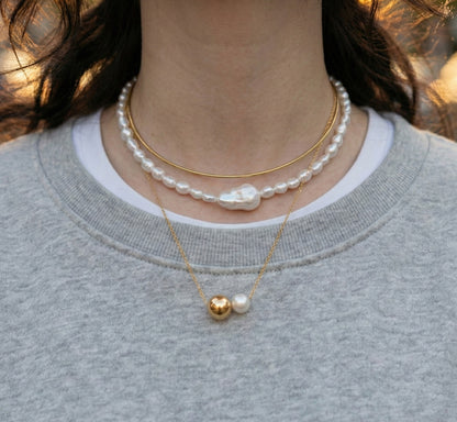 Woman wearing layered pearl and brass choker with gray knit sweater