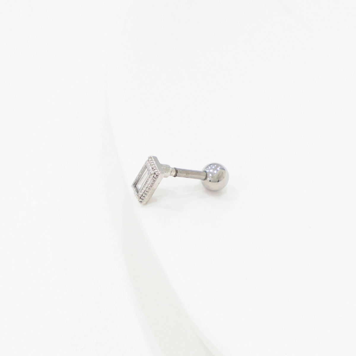 Single rectangular clear CZ barbell earring in a silver setting, placed on a white display.