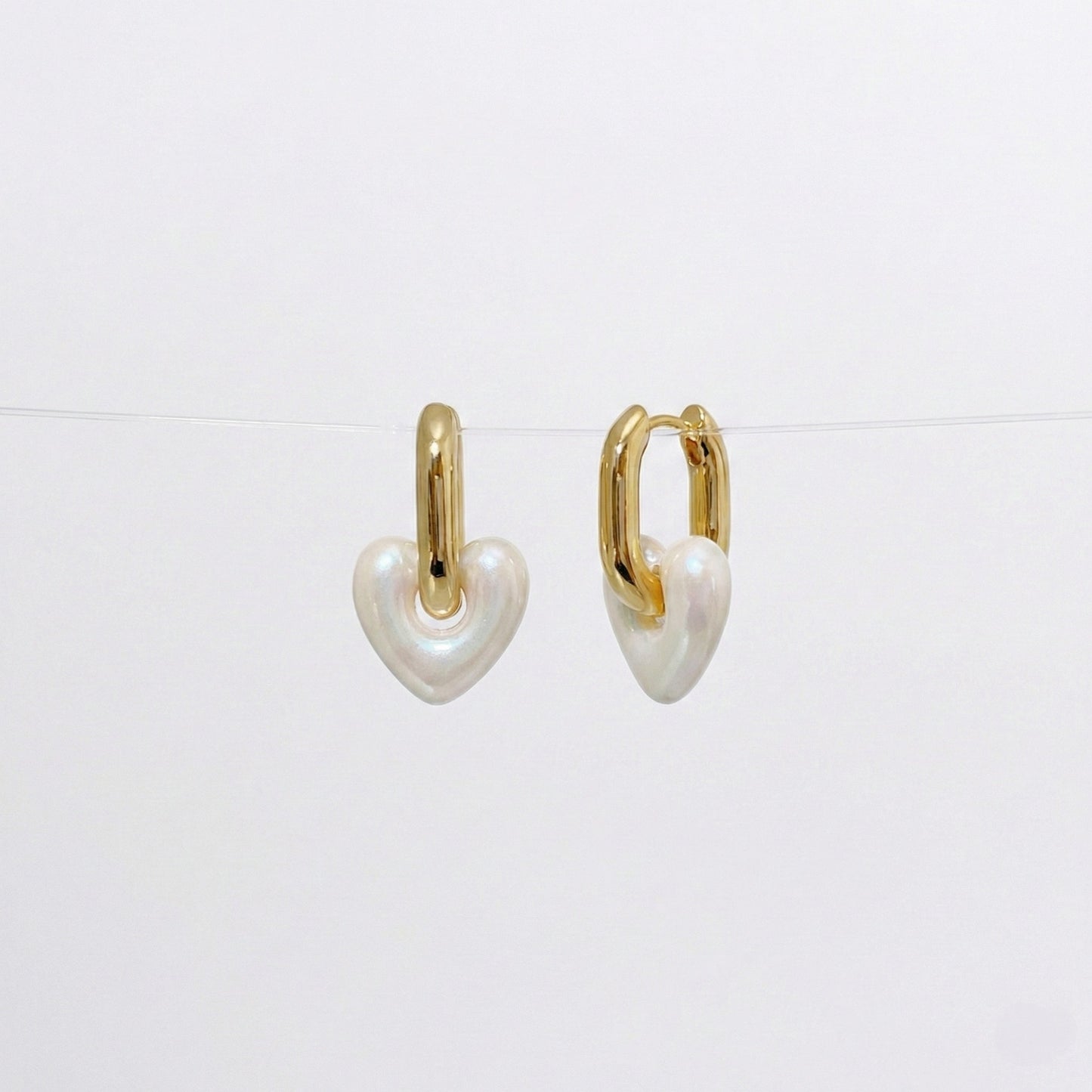 Pearl white heart charm earrings with glossy acrylic finish and gold huggie hoops
