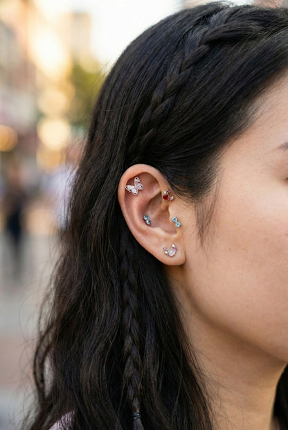Curated ear stack with butterfly helix piercing, red moon heart stud, blue bow tragus earring, and crystal lobe studs