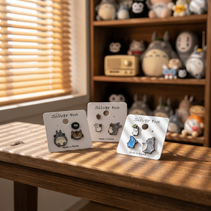 Three Studio Ghibli earring sets displayed on wooden table with collectibles background
