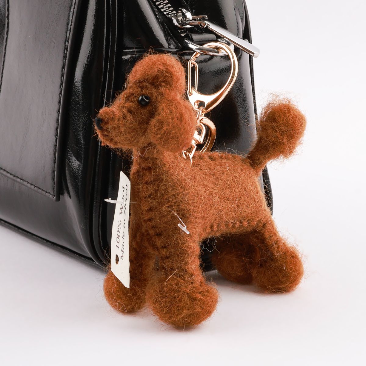 Close-up of brown wool poodle bag charm attached to black leather handbag with rose gold hardware
