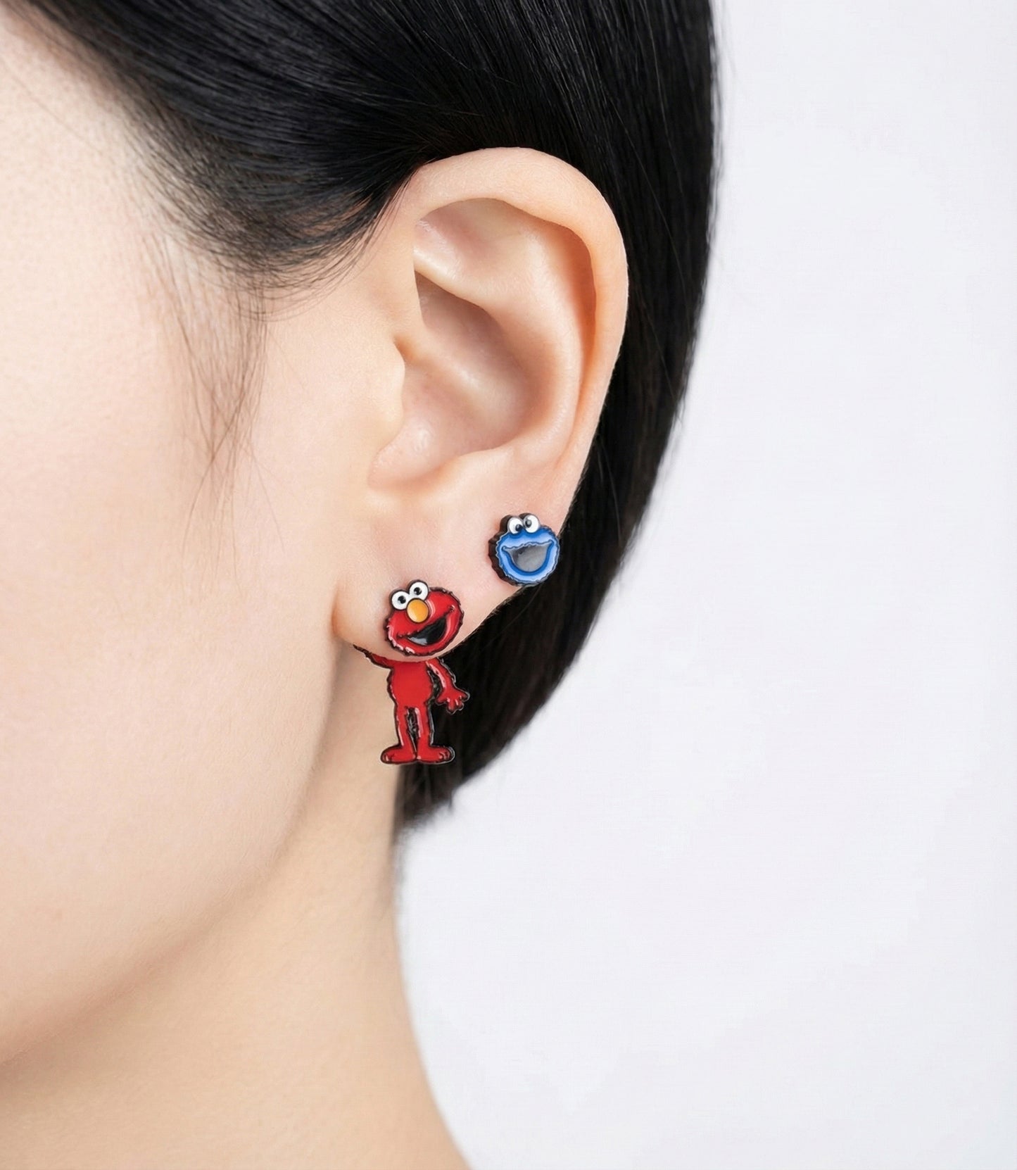 Elmo and Cookie Monster mismatched earrings styled on ear; Elmo full body dangles below, Cookie Monster head sits on lobe.