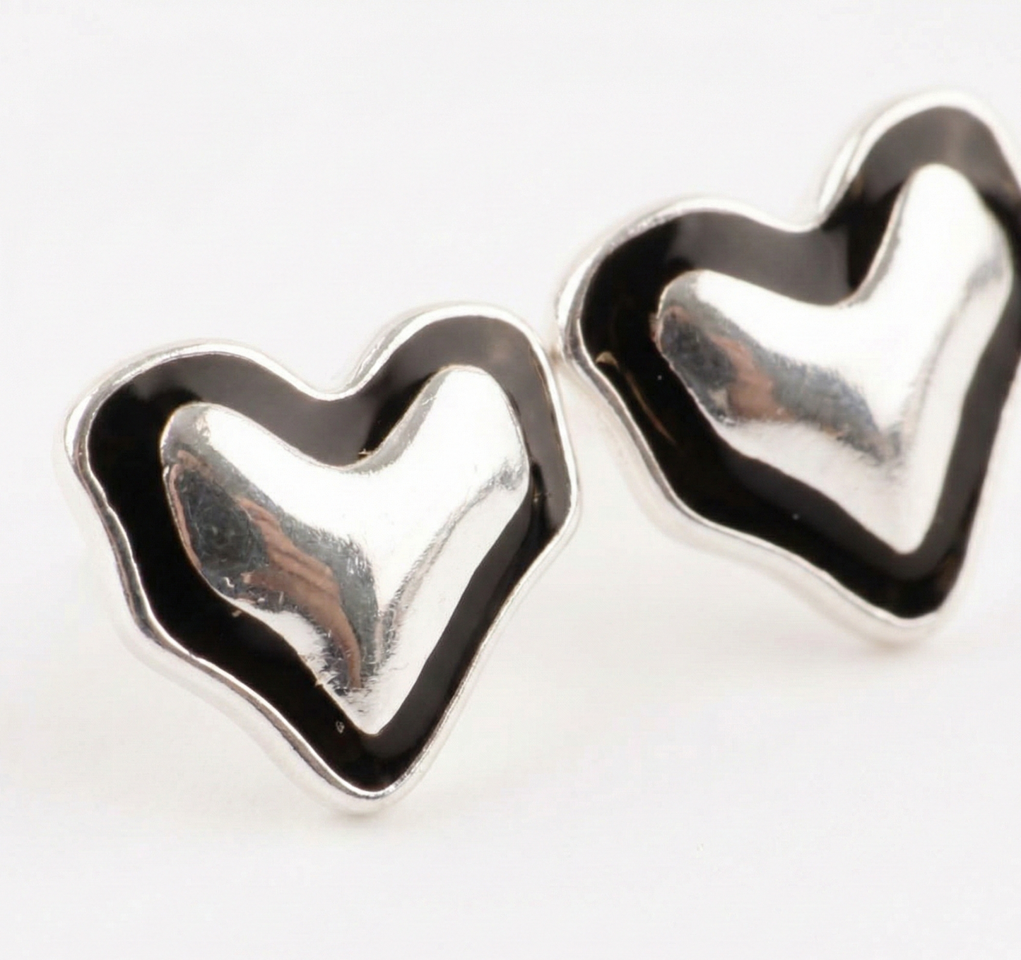 Macro detail of 925 sterling silver black enamel heart stud earrings pair showing mirrored silver surface and thick enamel border