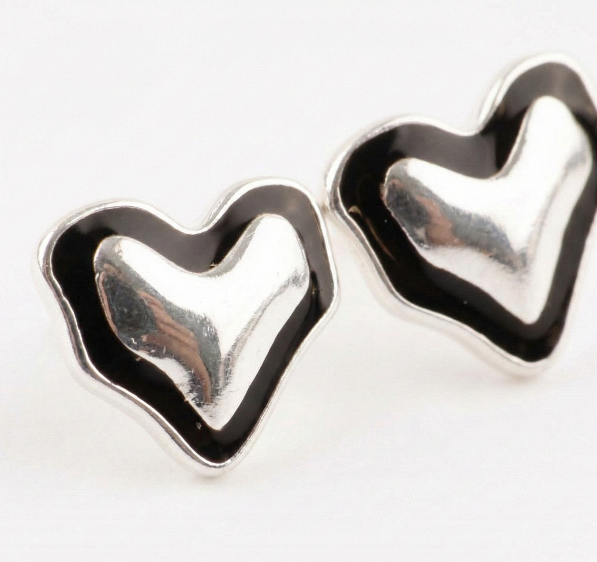 Macro detail of 925 sterling silver black enamel heart stud earrings pair showing mirrored silver surface and thick enamel border