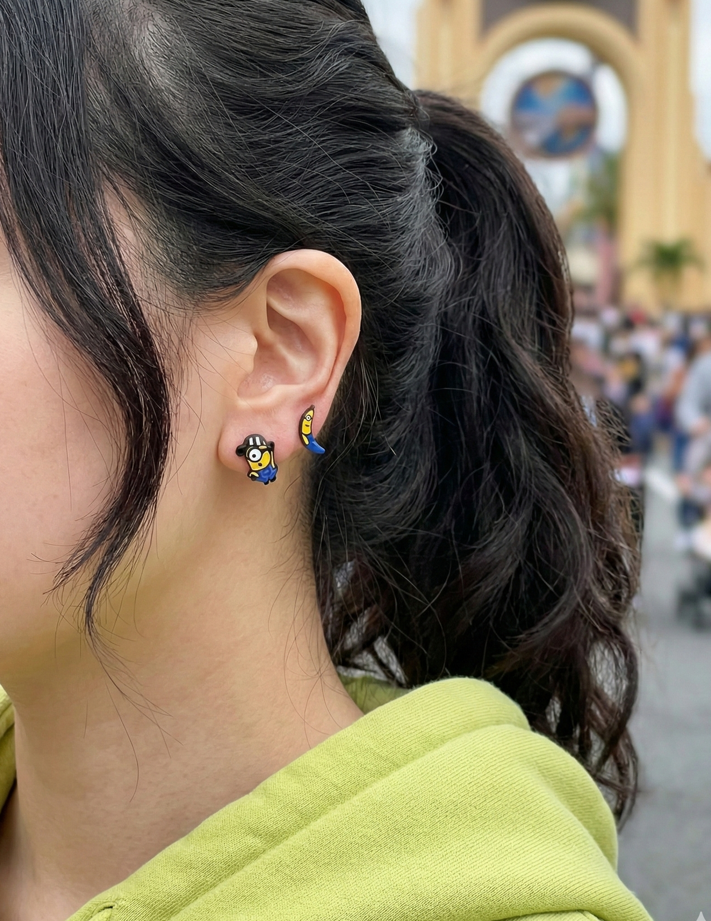 Woman wearing Minions mismatched earrings at Universal Studios theme park, banana and prisoner character studs visible on ear