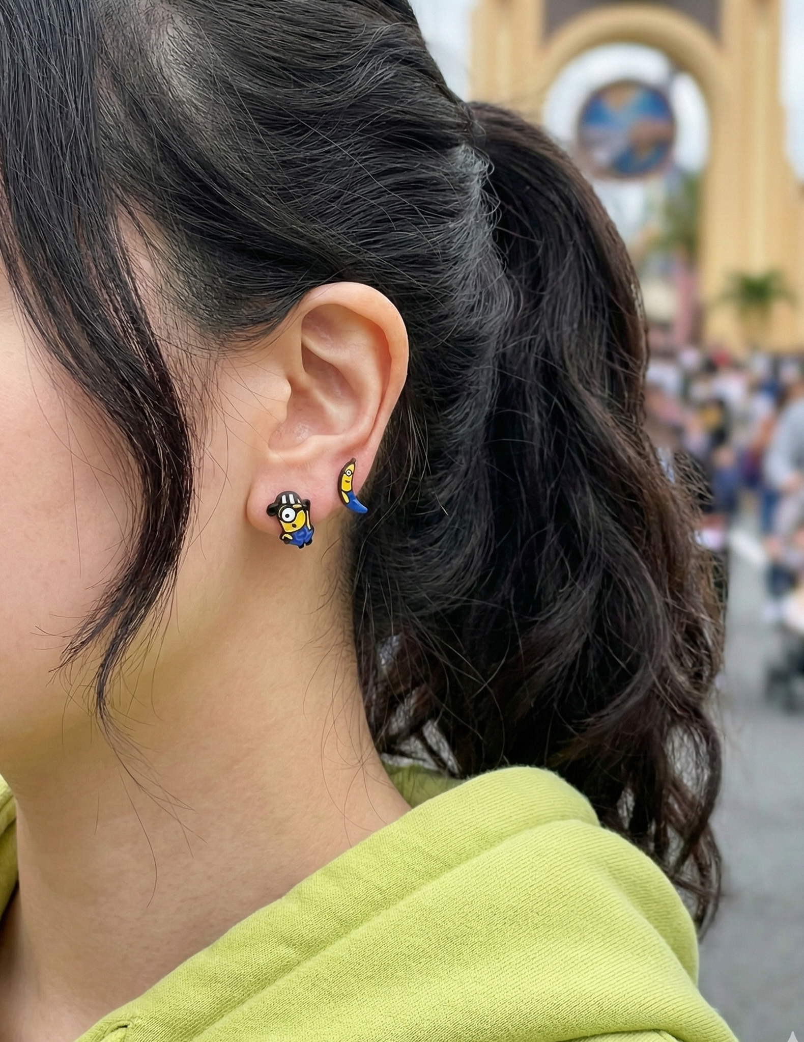 Woman wearing Minions mismatched earrings at Universal Studios theme park, banana and prisoner character studs visible on ear