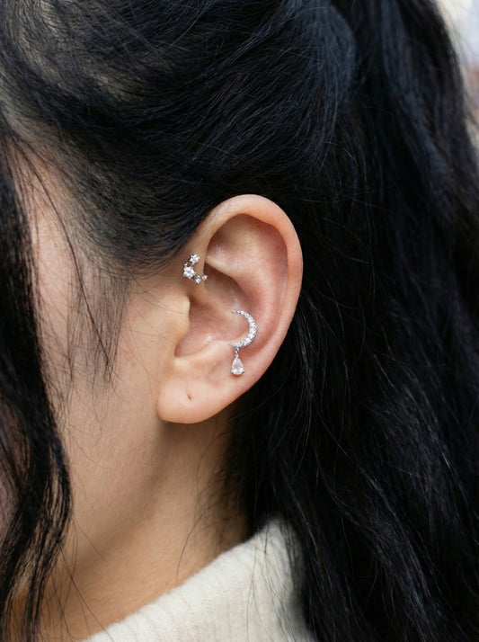 Layered ear piercings featuring crescent moon stud on conch and teardrop dangle on earlobe