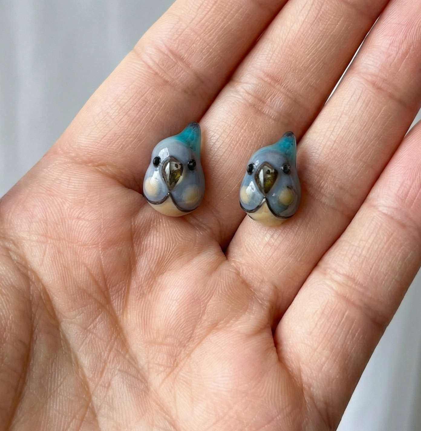 Blue parrot handmade earring pair resting on palm of hand showing size and enamel detail |