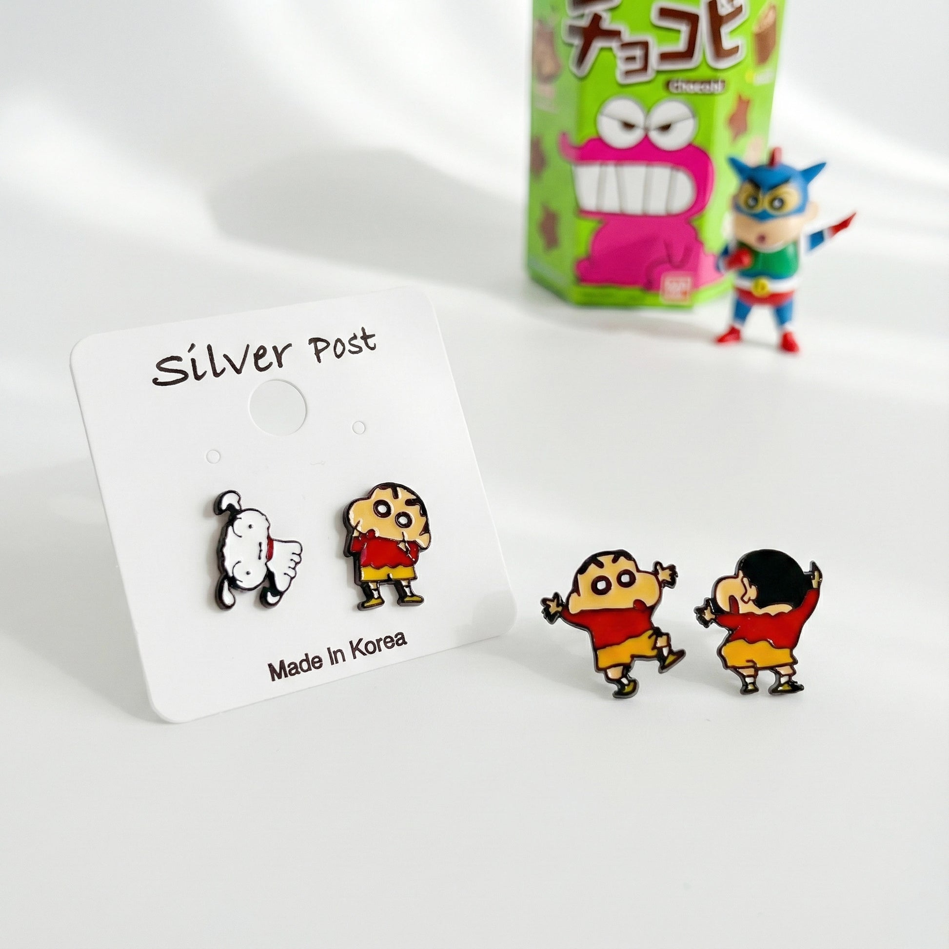 Crayon Shin-chan inspired stud earrings on a ‘Silver Post’ card featuring a white dog and a child in a red and yellow outfit, styled with toys in the background.