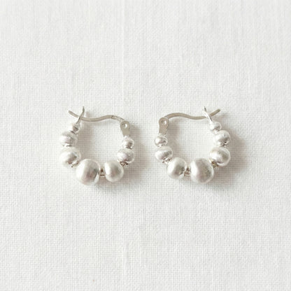 Pair of silver beaded hoop earrings on white linen background, displaying textured spherical beads in graduated sizes, 925 sterling silver posts hypoallergenic, lightweight comfortable fit for sensitive ears