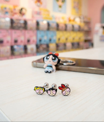 Three sleeping Powerpuff Girls barbell stud earrings displayed on table - Blossom Bubbles Buttercup with pink packaging background