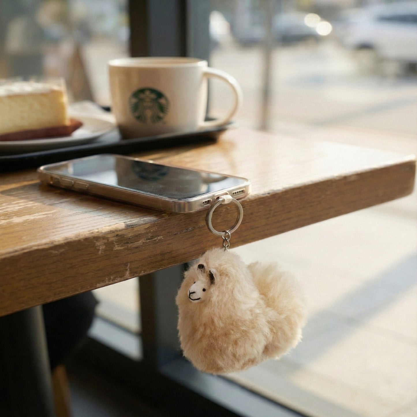 Beige alpaca keychain attached to smartphone on wooden table