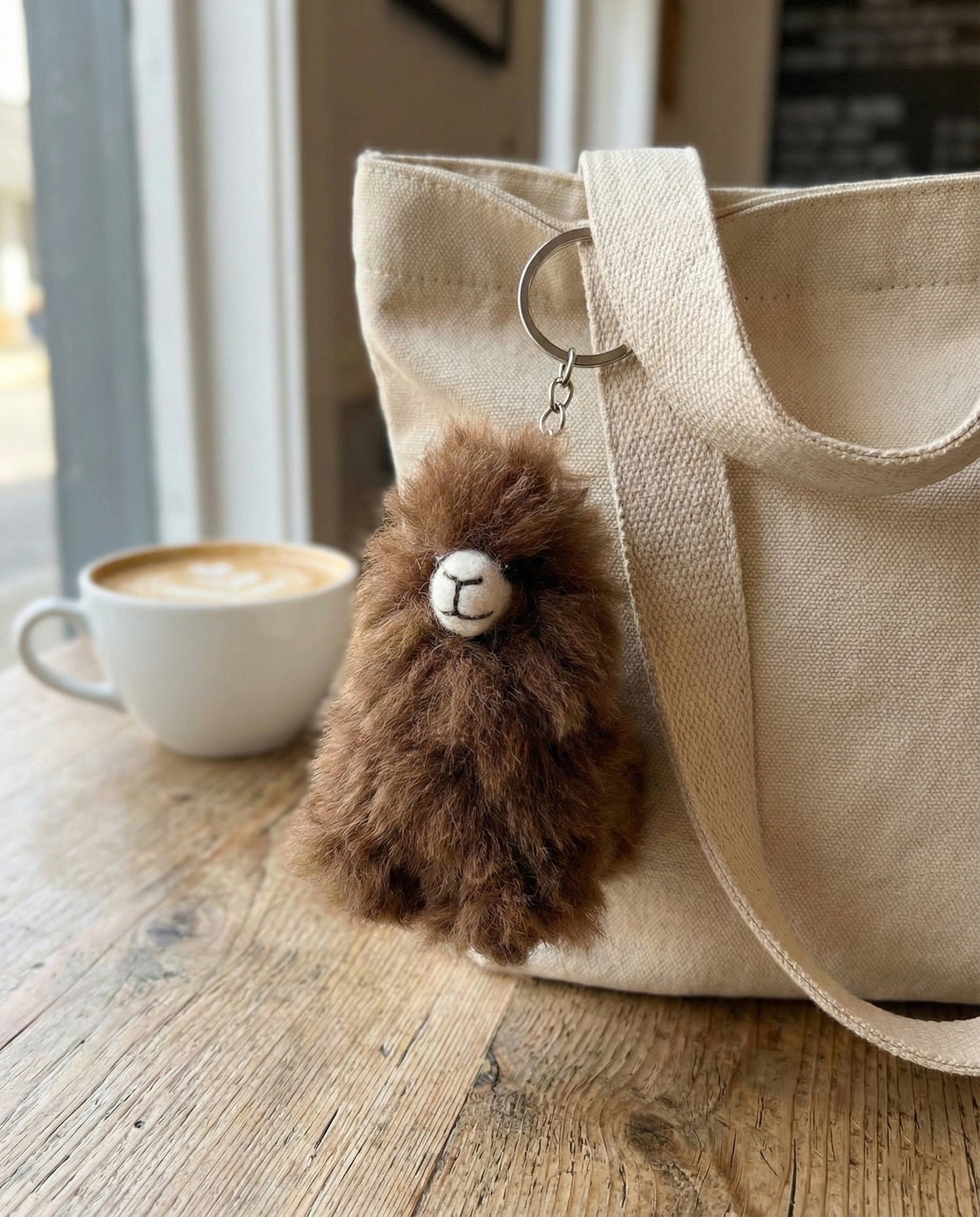 Alpaca fur keychain charm attached to beige canvas tote bag with latte on wooden table