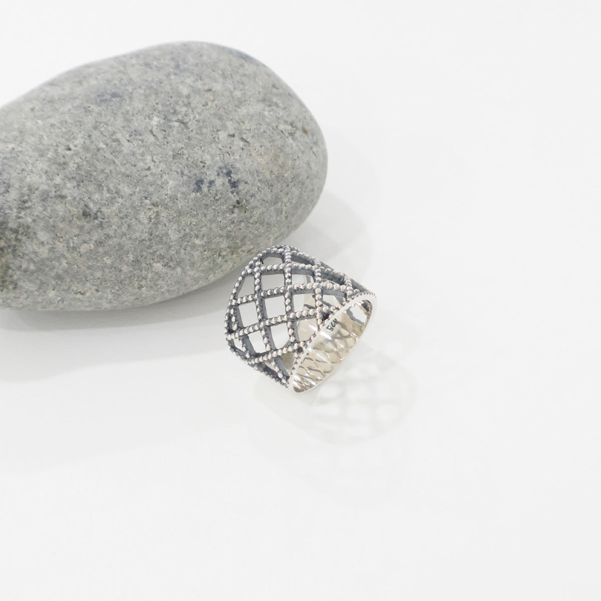 Single 925 sterling silver lace lattice bold wide band ring lying on white surface next to gray stone, showing beaded diamond grid pattern and 925 stamp