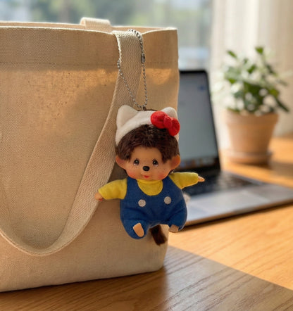 Monchhichi keychain hanging on beige canvas tote bag handle in cafe setting