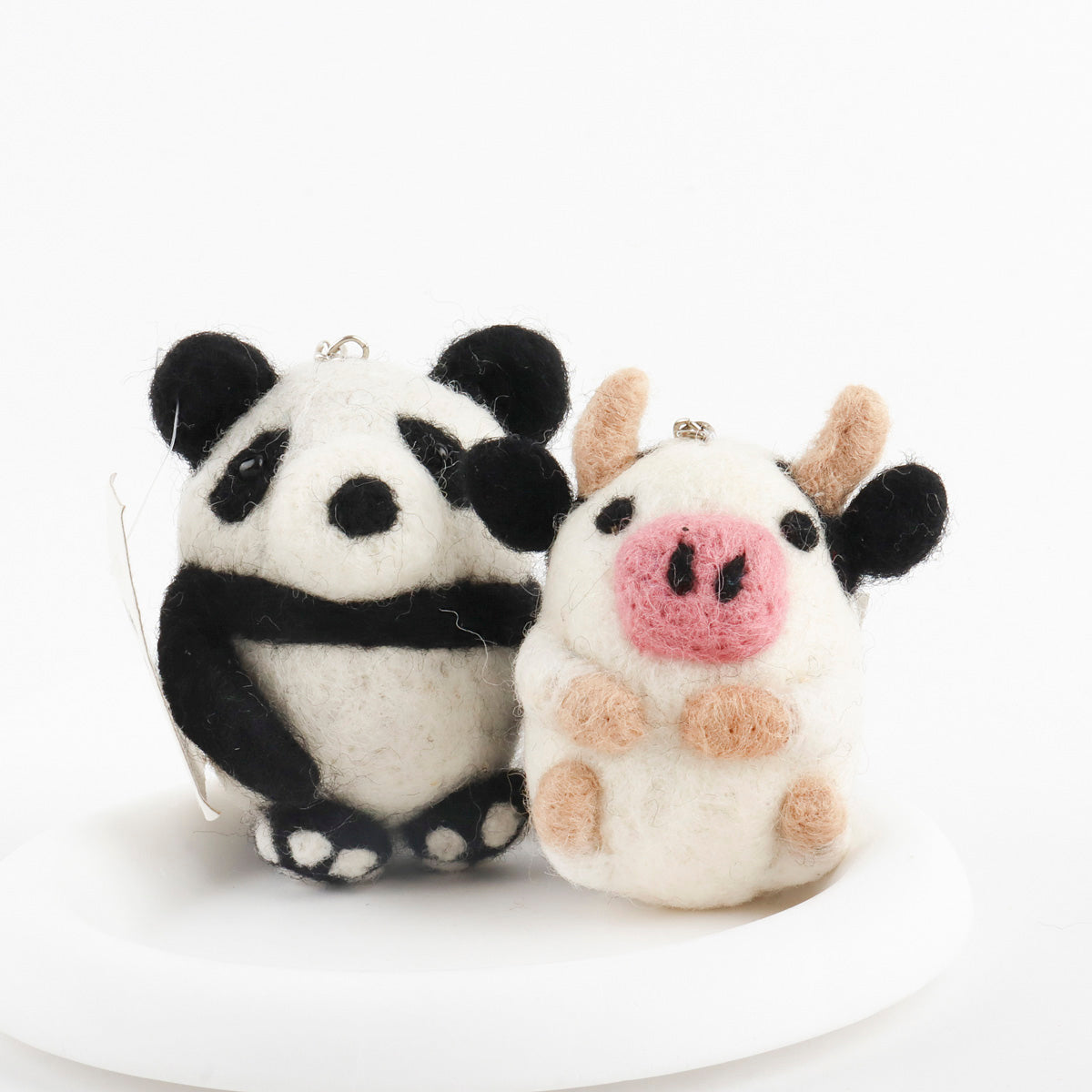 Close-up of handmade wool felt panda and cow keychains showing detailed needle felting texture