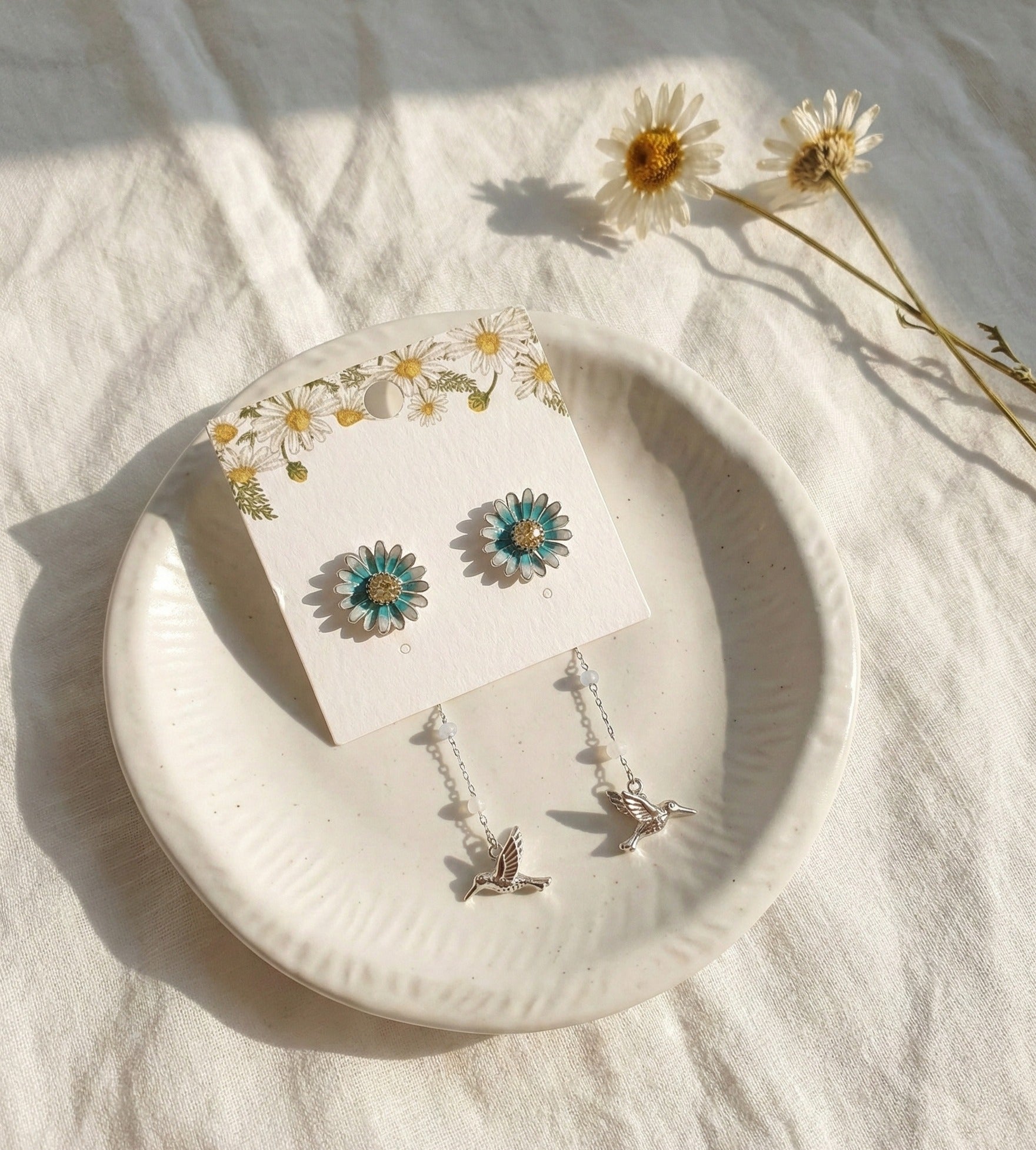 Silver daisy flower earrings with hummingbird drop on white plate with real daisies