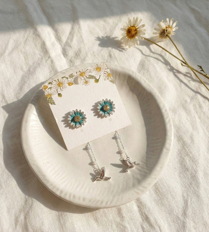 Silver daisy flower earrings with hummingbird drop on white plate with real daisies