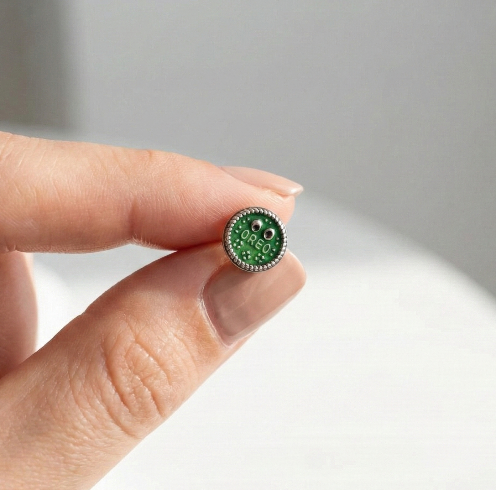 Hand holding green Oreo surgical steel piercing showing actual size comparison