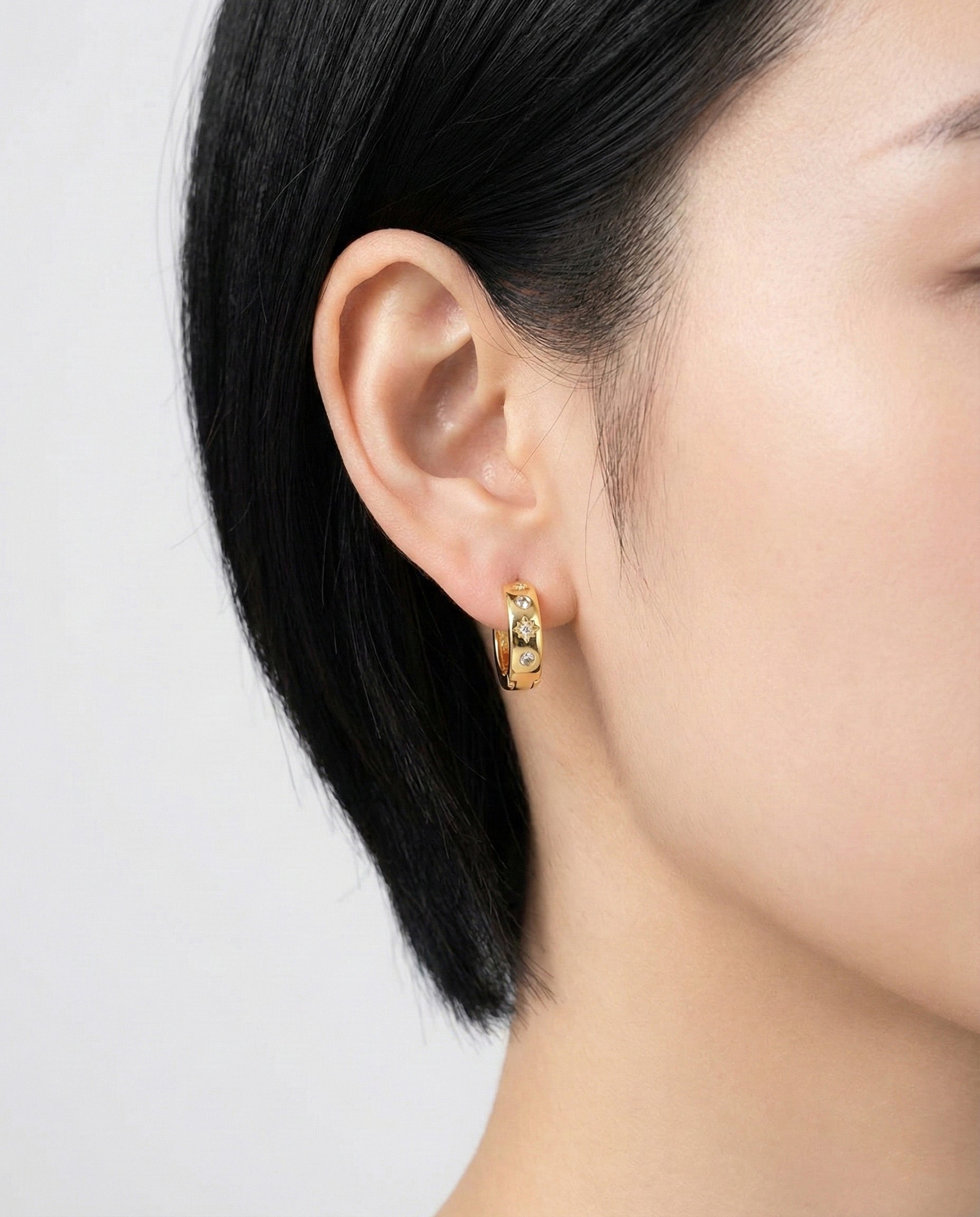 Yellow gold huggie earrings with star-shaped cubic details worn on the left ear, straight side view.