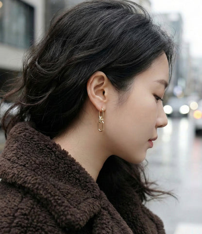 Woman wearing gold chain knot drop earrings with brown teddy coat, side profile view