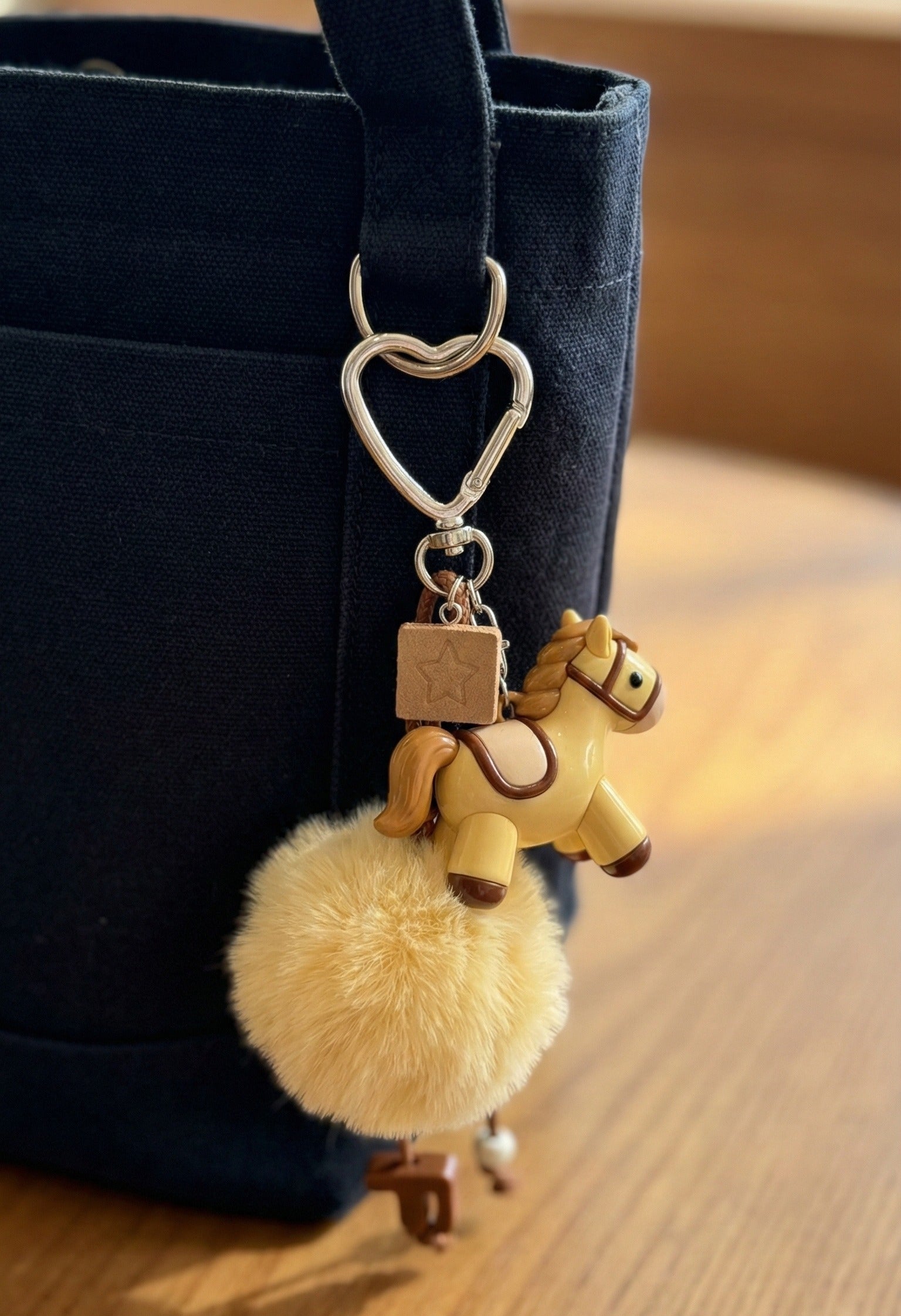 Cream pony keychain attached to navy blue canvas tote bag with heart clasp