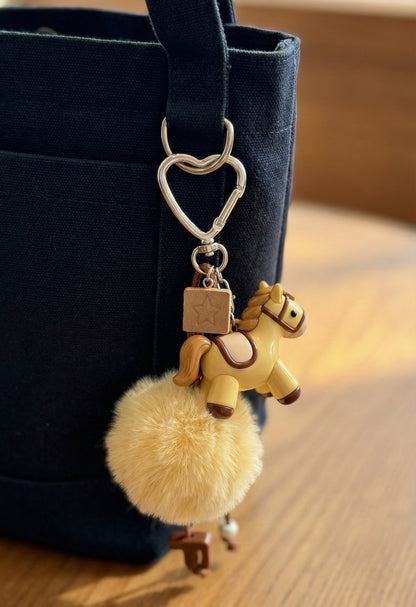 Cream pony keychain attached to navy blue canvas tote bag with heart clasp
